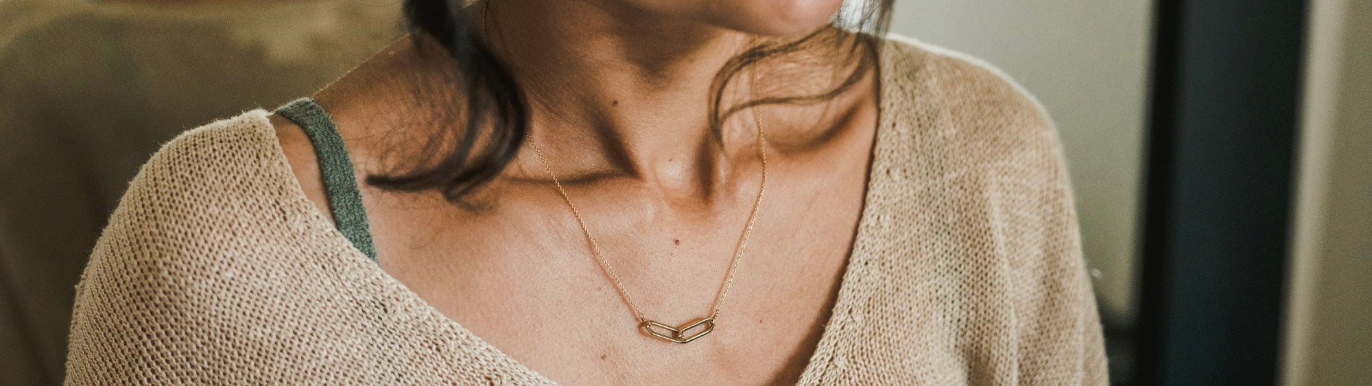 Close-up of a person wearing a beige knit sweater and a geometric gold necklace.