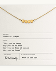 The May You Be Happy Necklace by Becoming Jewelry is a gold necklace with five beads on a card inscribed with a Buddhist prayer for happiness, health, safety, and love. Published in the USA.