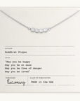 The May You Be Happy Necklace by Becoming Jewelry features pearl-like beads on a card with a Buddhist prayer for happiness, health, safety, and love.