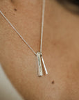 A close-up of a person's neck wearing the top-selling Through Thick & Thin Necklace from Becoming Jewelry, adorned with two slim rectangular pendants.