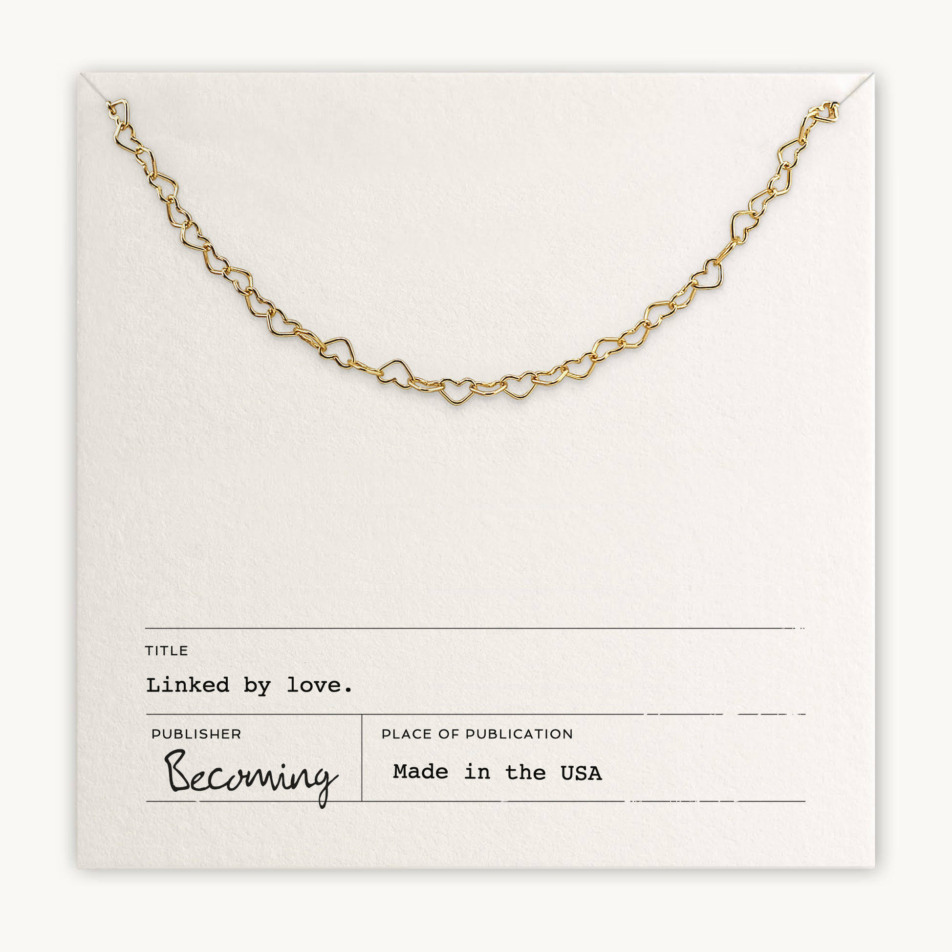 A delicate gold heart-shaped necklace, the "Heart Chain Necklace," is showcased on a "Linked by Love" card and crafted with care by Becoming Jewelry in the USA.