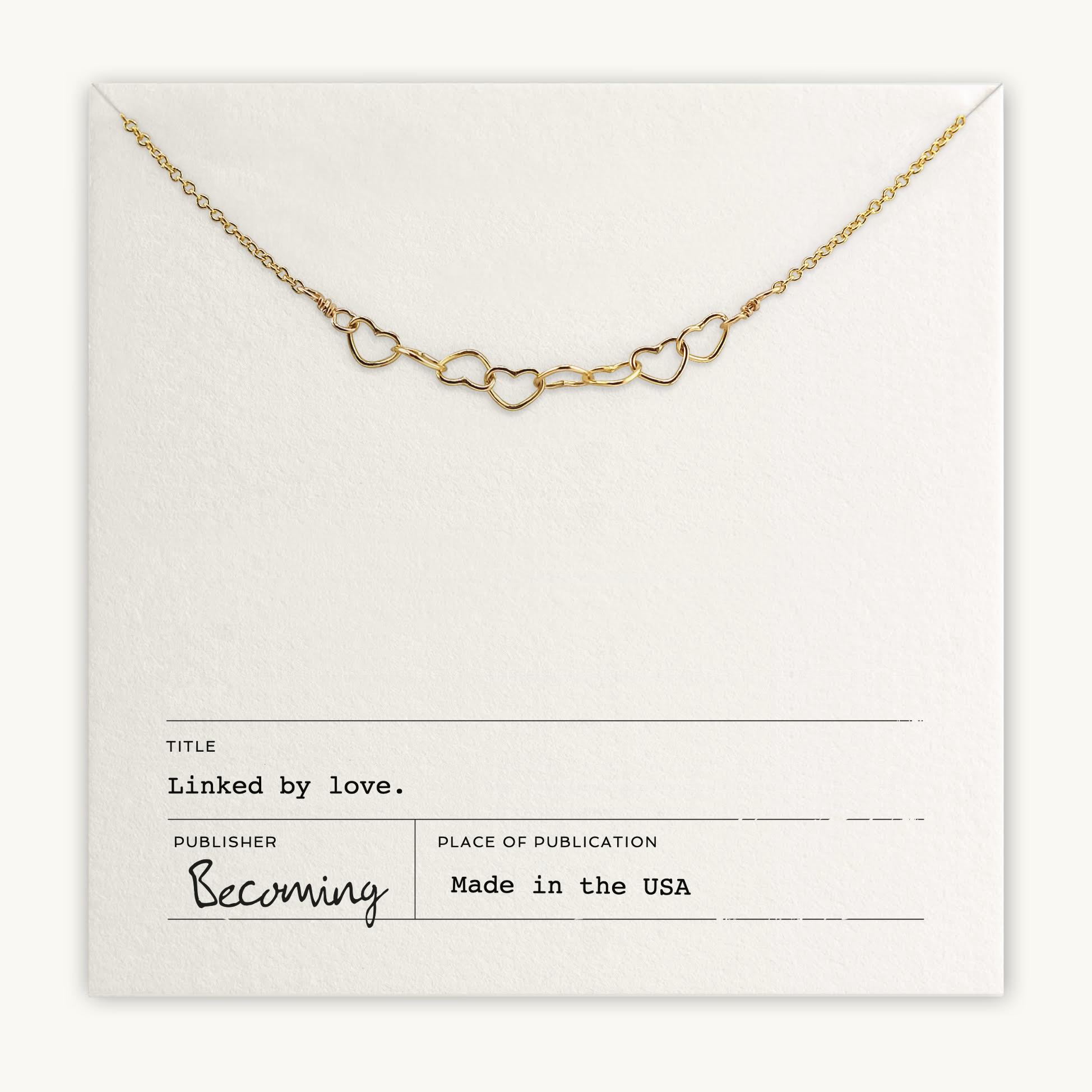 The Heart Links Necklace by Becoming Jewelry features interconnected heart shapes elegantly gleaming on a textured card. It includes the text "Linked by love," capturing enduring affection and connection, with "Becoming" and "Made in the USA" proudly displayed.