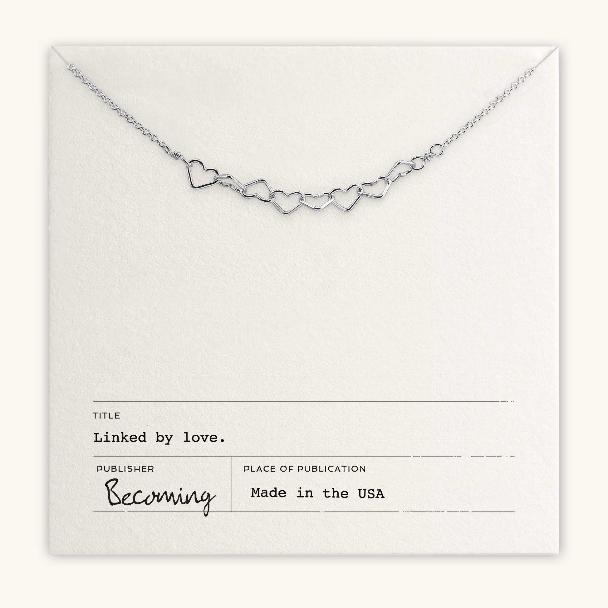 The Heart Links Necklace from Becoming Jewelry features silver heart links on a "Linked by Love" white card, marked "Made in the USA." This elegant chain embodies love's essence through its graceful design.