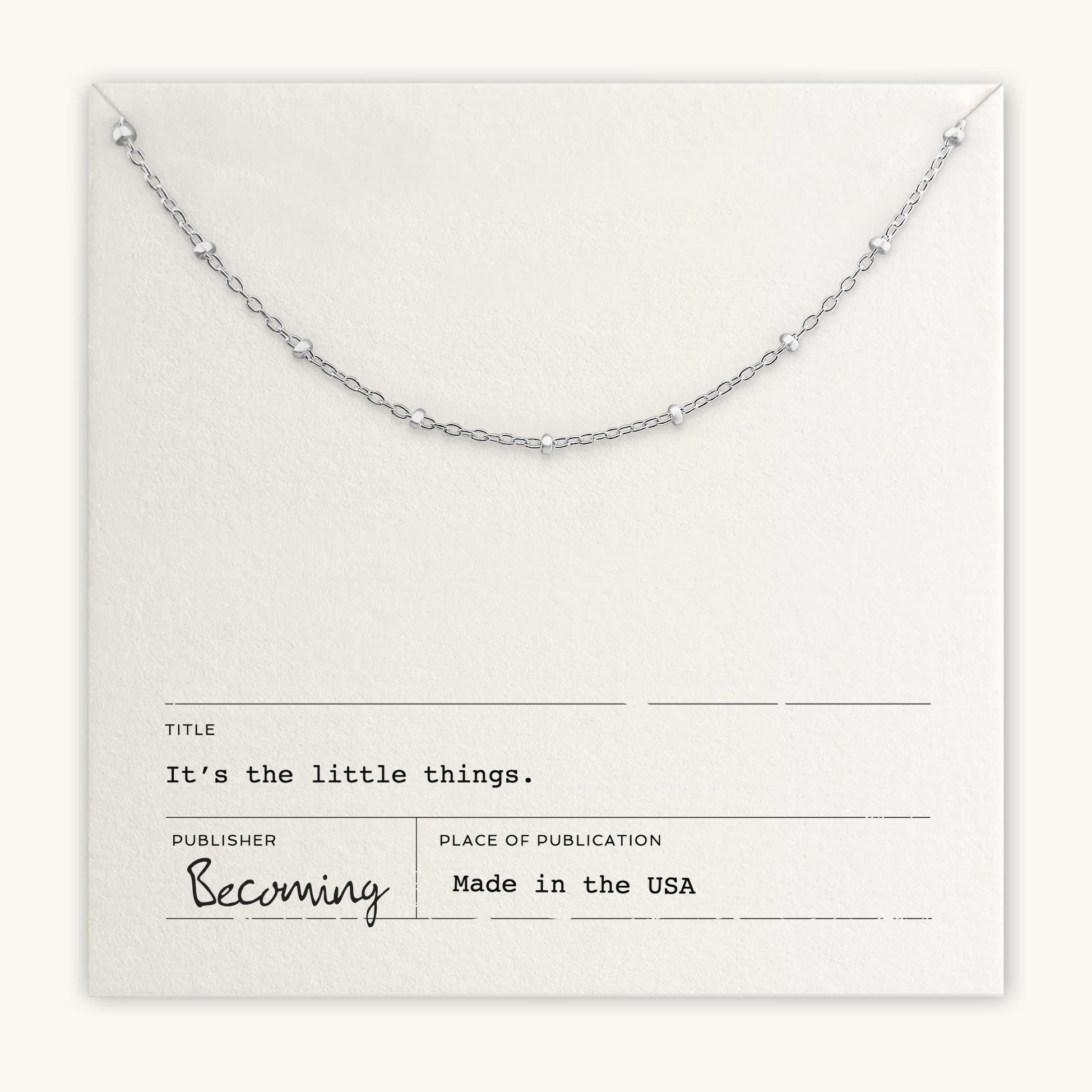 The Little Things Necklace by Becoming Jewelry is a delicate beaded silver chain resting on a card that reads "It's the little things." Made in the USA, this piece makes a meaningful gift and daily reminder of life's simple joys.