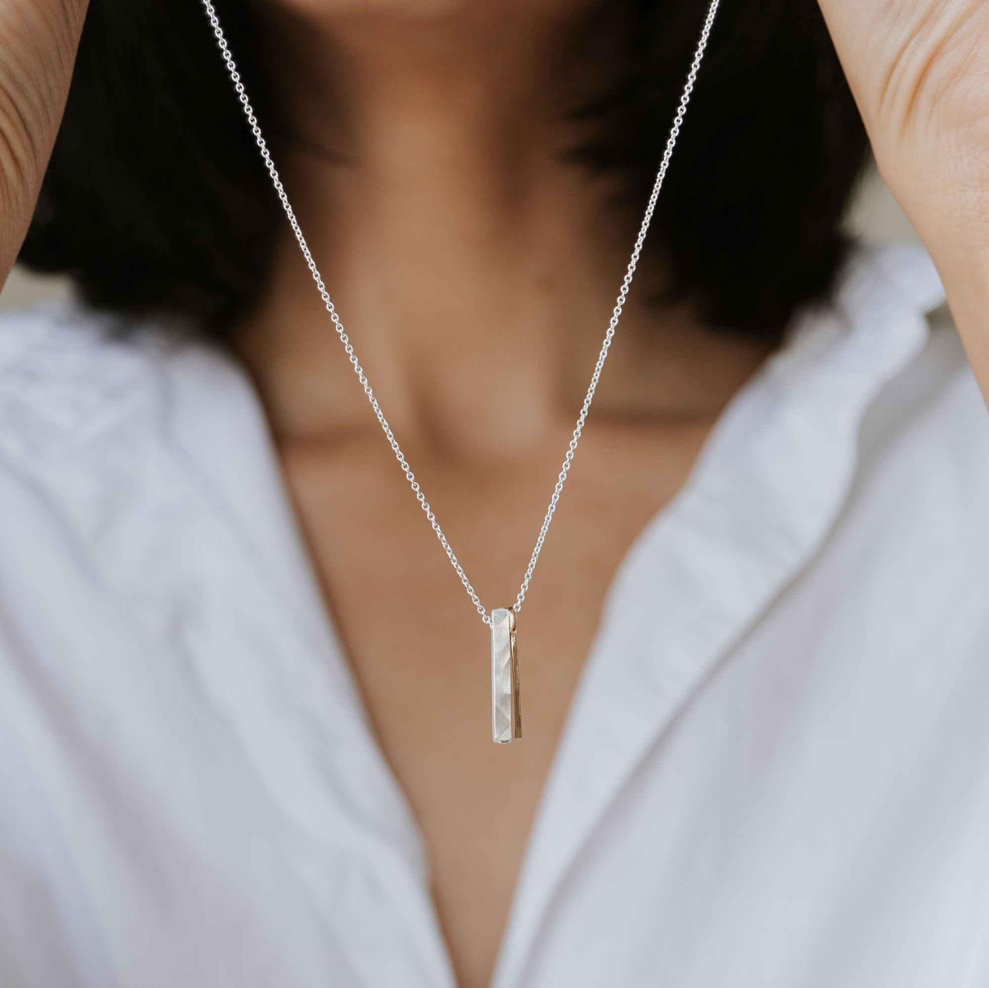 A person holds up the best-selling Through Thick &amp; Thin Necklace from Becoming Jewelry, featuring a vertical rectangular pendant, showcasing it against a white shirt—a perfect gift symbolizing enduring connections.