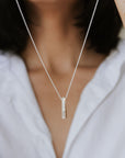 A person holds up the best-selling Through Thick & Thin Necklace from Becoming Jewelry, featuring a vertical rectangular pendant, showcasing it against a white shirt—a perfect gift symbolizing enduring connections.