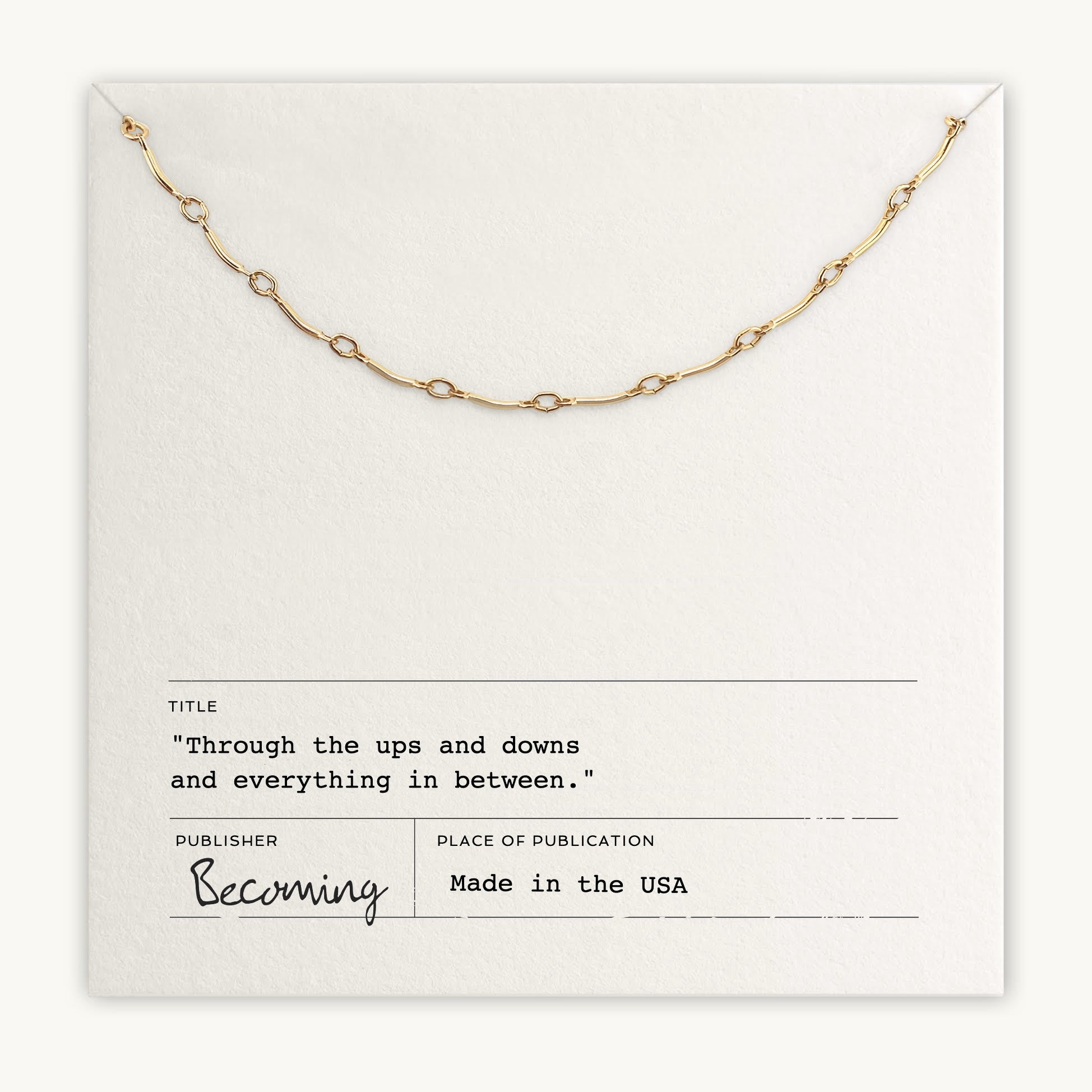 A delicate "Ups & Downs Necklace" by Becoming Jewelry is elegantly displayed on a white background, featuring the text "Through the ups and downs and everything in between," highlighting resilience, with publication details at the bottom.