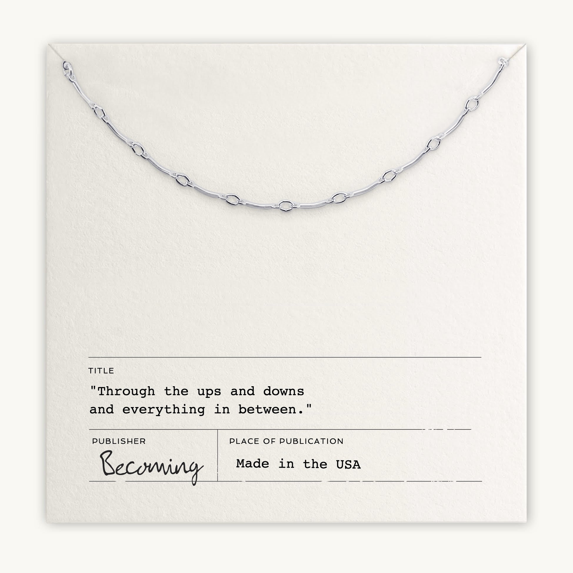 A minimalist Ups & Downs Necklace from Becoming Jewelry, beautifully displayed on a textured white card with the message "Through the ups and downs and everything in between." Made in the USA, this meaningful gift symbolizes resilience and support.