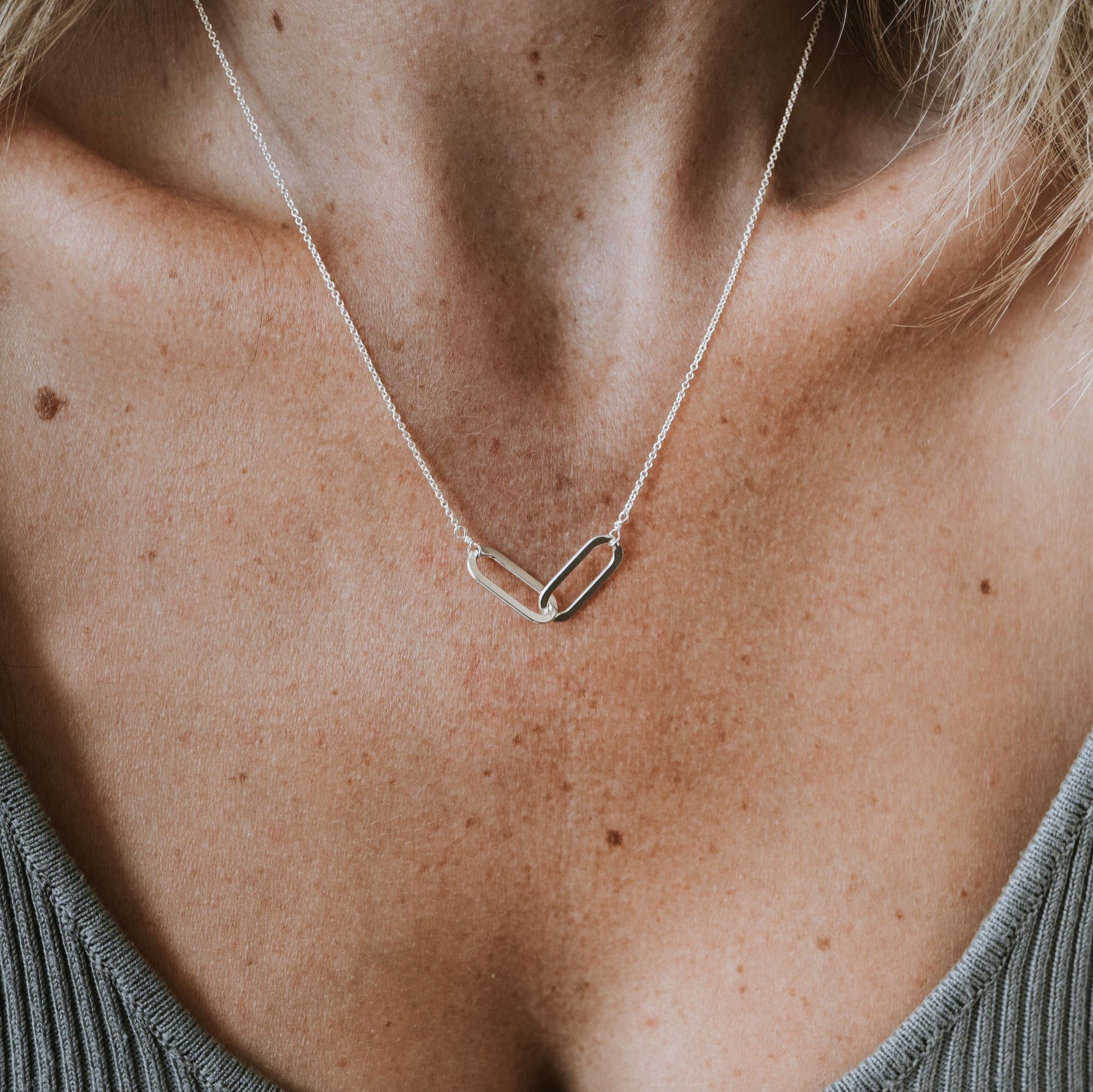 Close-up of a person wearing the Linked Together Necklace by Becoming Jewelry, a silver piece with a minimalist design resembling interlocking geometric shapes, symbolizing connection and making it an ideal gift.