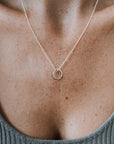 Close-up of a person's neck wearing the True Friends Necklace by Becoming Jewelry, featuring two mixed metal, textured circles as a pendant, shown against a ribbed grey top.