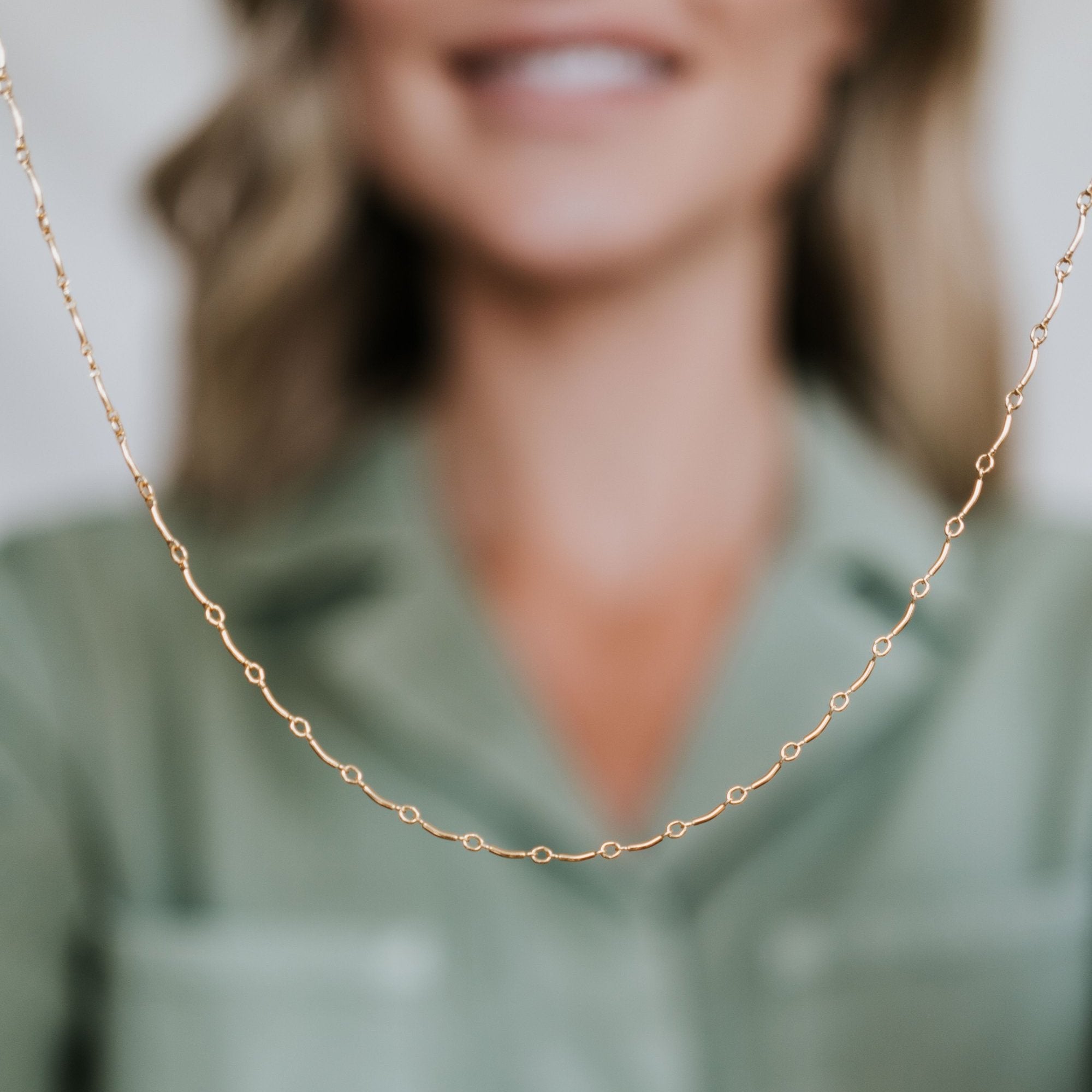 A person wearing a light green shirt holds up a delicate gold chain necklace, displaying it up-close. This Ups & Downs Necklace from Becoming Jewelry makes for a meaningful gift, symbolizing resilience and support.