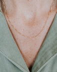 Close-up of a person wearing a light green textured blouse and a delicate gold chain necklace, reminiscent of the Ups & Downs Necklace by Becoming Jewelry—an emblem of resilience and support.