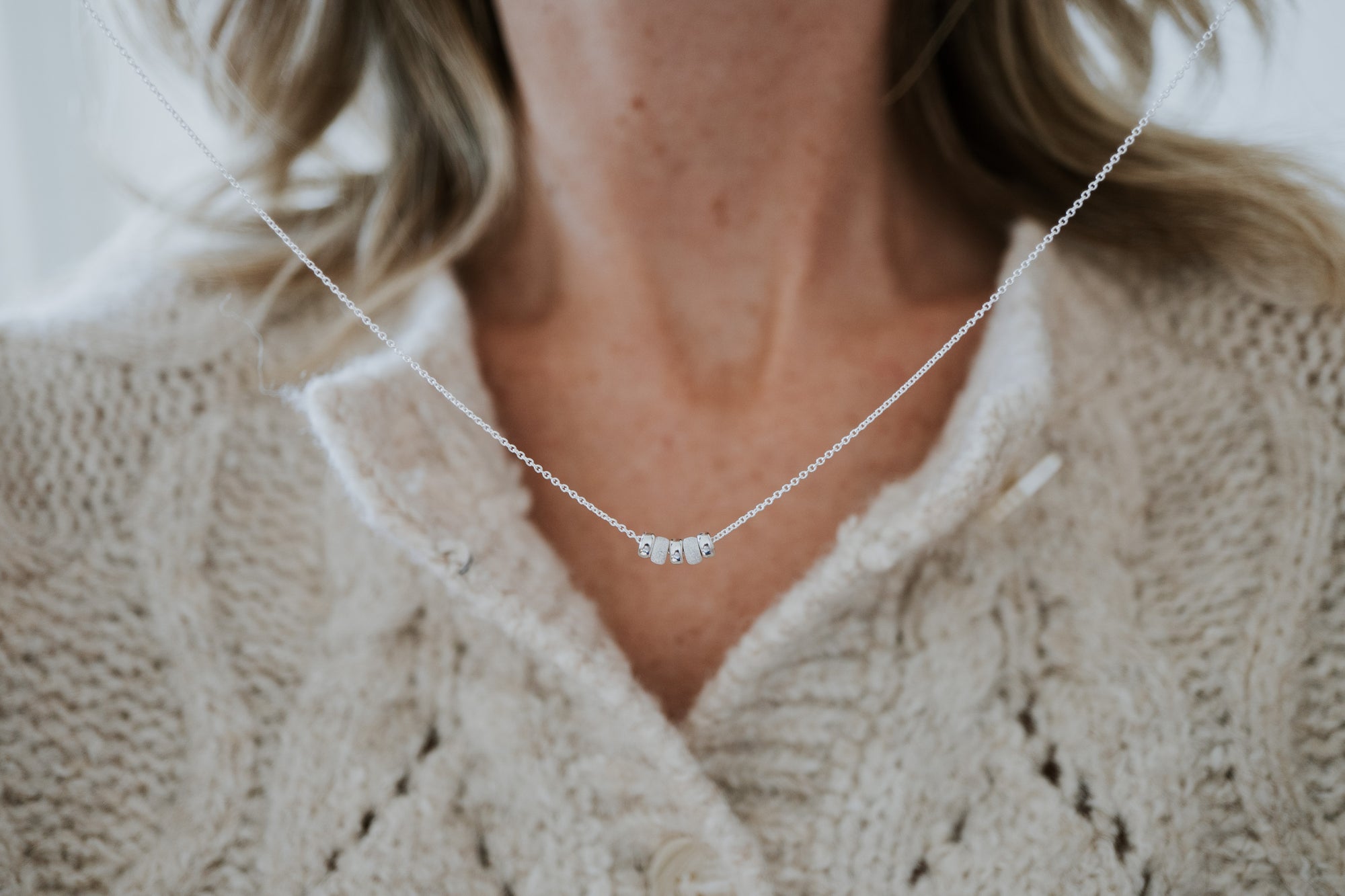 Model holding Sterling Silver version of My Wish For You necklace with cream knitted sweater background